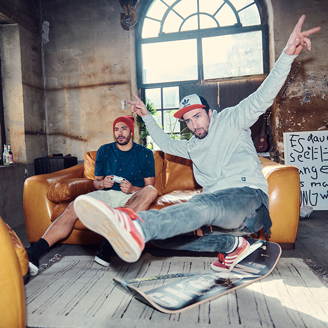 Two men in a casual setting with one sitting on a couch and the other doing a trick on a slackboard.
