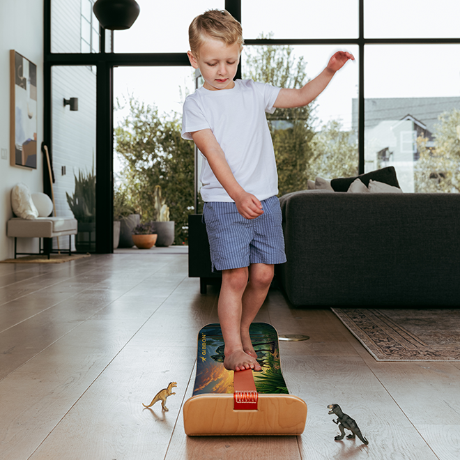 Child standing on a small dino slackboard with dinosaur graphics in a living room.