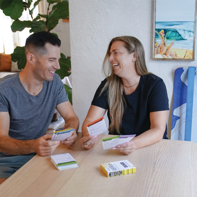 Two people sitting at a table with a deck of GIBBON SlackBoard Exercise cards, smiling and engaged in a conversation.